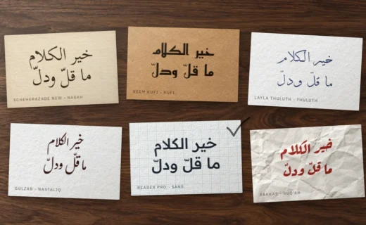 Six cartes sur un bureau en noyer, le même proverbe arabe composé dans six styles de police, l'une cochée au crayon